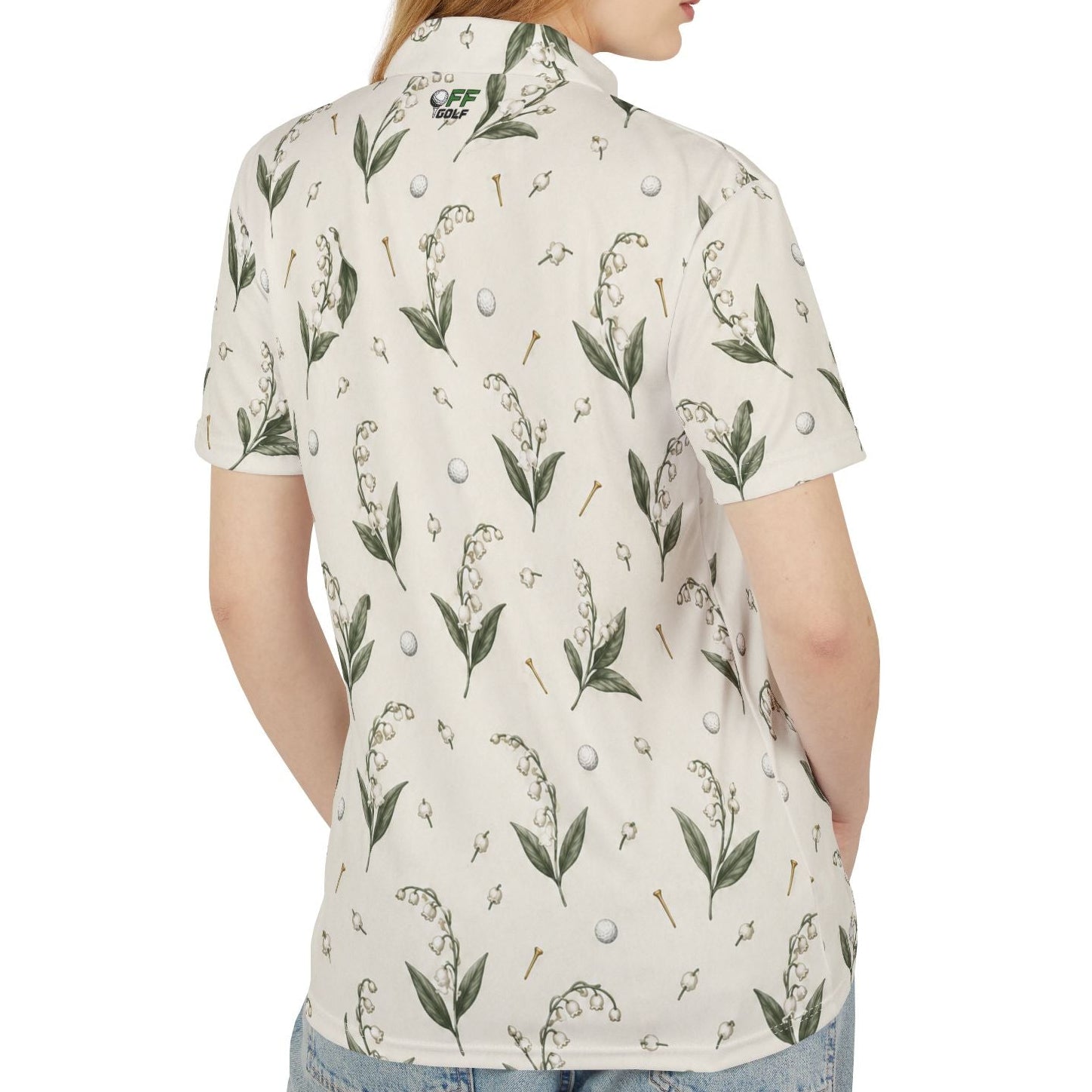 A woman shown from the back wearing a short-sleeve collared shirt with an allover botanical print of green leaves, lily of the valley flowers, golf tees, and white golf balls on an off-white background. The shirt features a green and white 'Golf Club' logo printed inside the collar.