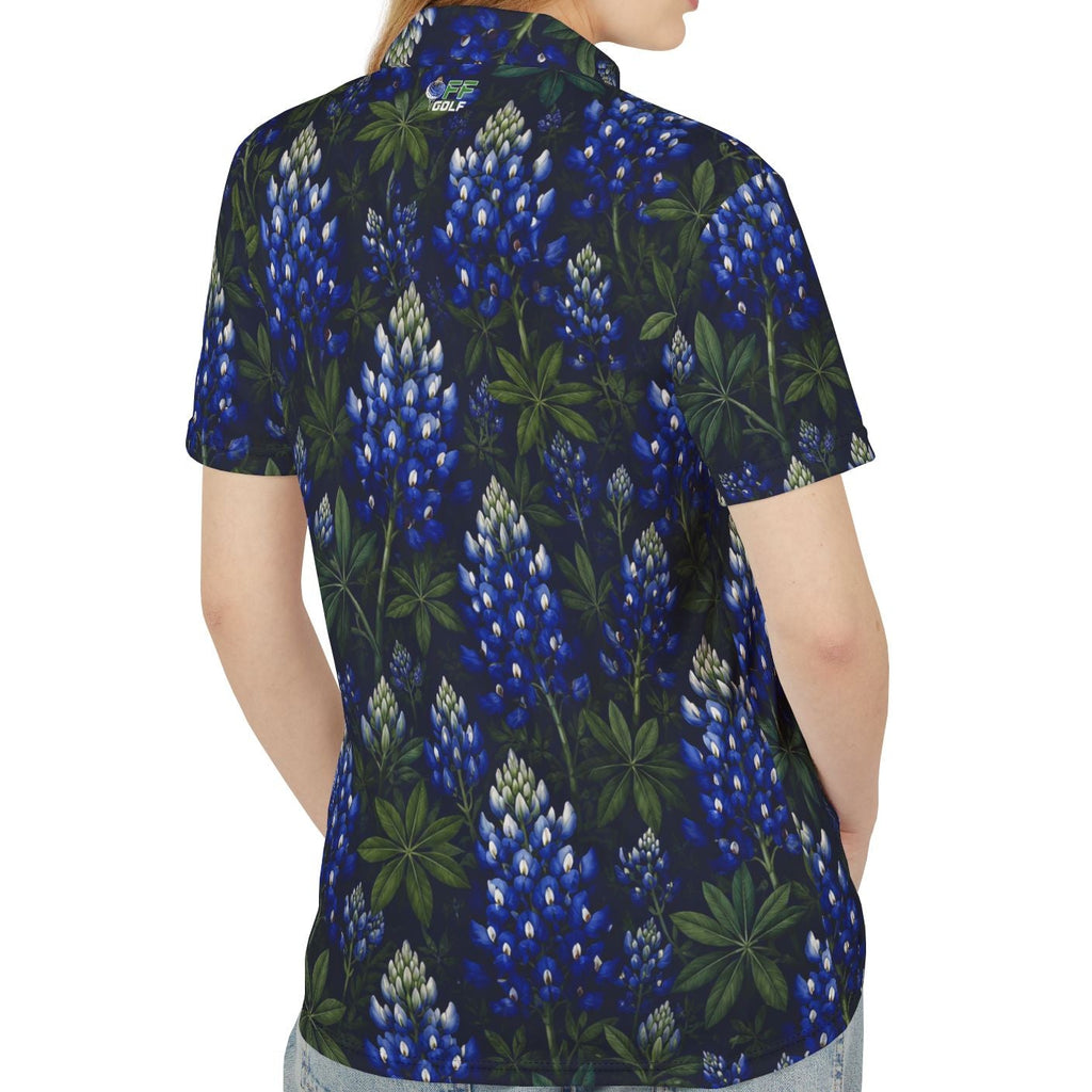 A woman shown from the back wearing a short-sleeve button-up shirt with a dark navy blue and green botanical pattern featuring blue flowers, paired with light-wash jeans, against a plain white background.