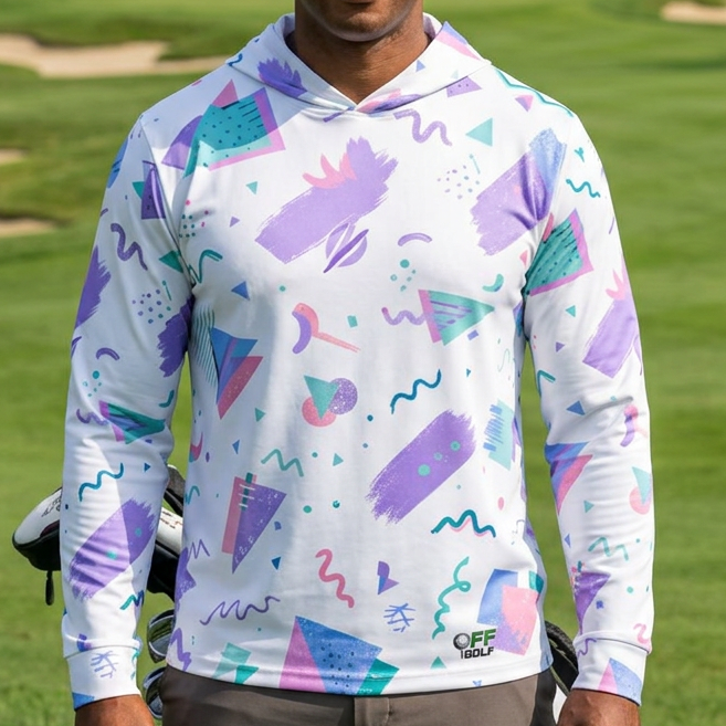 A man standing on a golf course wearing a white long-sleeve hoodie with a colorful 1980s-style geometric print in purple, teal, and pink. He is holding a golf bag, with trees and sand bunkers in the background.