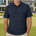 A smiling man stands on a manicured golf course wearing a navy blue short-sleeve polo shirt with a small beige star pattern, paired with khaki pants. A modern house is visible in the background.