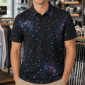 A smiling man wearing a dark navy short-sleeve polo shirt with a colorful galaxy print stands inside a retail store. The shirt features a pattern of stars, dots, and nebulae in shades of blue, purple, orange, and yellow.