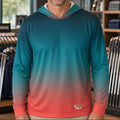 A smiling man wearing a long-sleeve hooded performance shirt with a teal-to-pink gradient, standing inside a golf retail store.