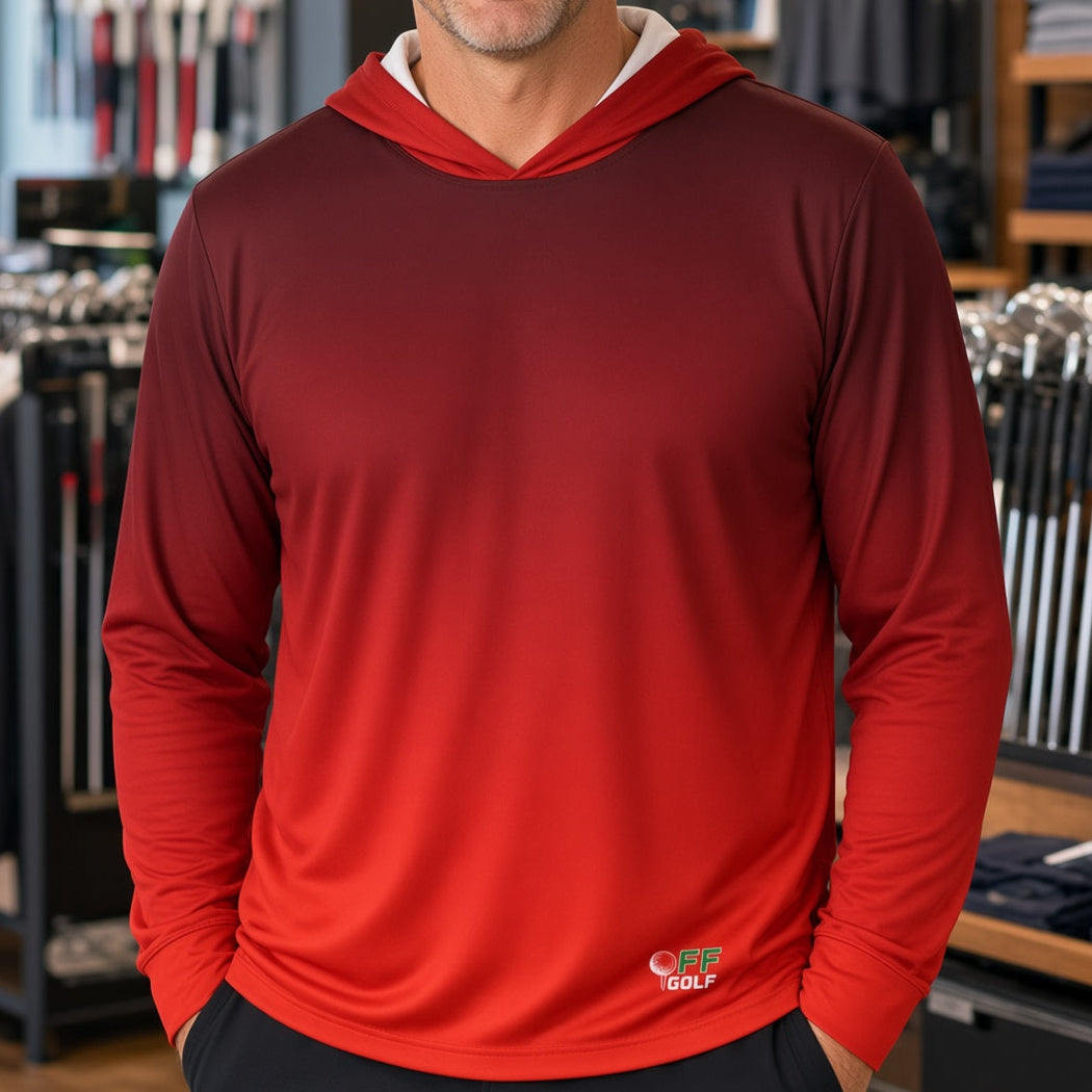 A smiling man wearing a red long-sleeve hooded performance shirt stands inside a retail store. The shirt has a darker red hood and a small white and green logo near the lower left hem that reads 'GOLF'.