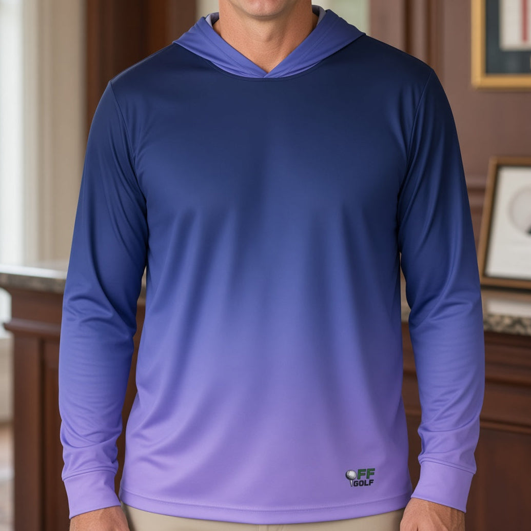 A man wearing a long-sleeve gradient hoodie shirt that transitions from dark blue at the top to light purple at the bottom, standing in a warmly lit indoor office or lobby setting.