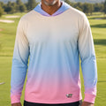 A smiling man wearing a long-sleeve gradient hoodie with a pastel color transition from cream to light blue and pink, standing on a golf course.