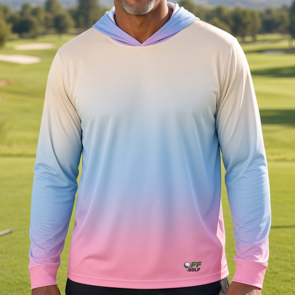 A smiling man wearing a long-sleeve gradient hoodie with a pastel color transition from cream to light blue and pink, standing on a golf course.