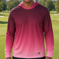 A man smiling on a golf course wearing a long-sleeve hooded performance shirt with a pink-to-magenta gradient.