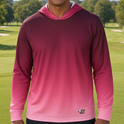 A man smiling on a golf course wearing a long-sleeve hooded performance shirt with a pink-to-magenta gradient.