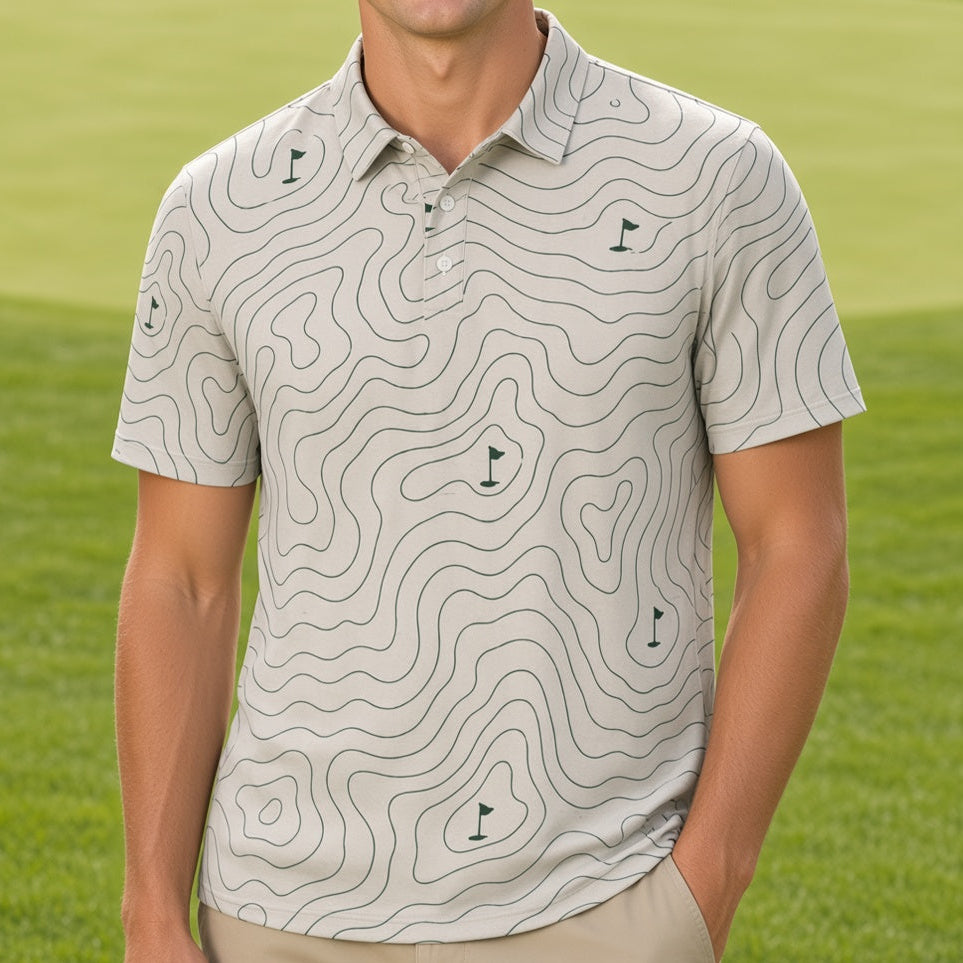A smiling man stands on a golf course wearing a short-sleeve polo shirt with a light beige and white topographic contour pattern and khaki pants.