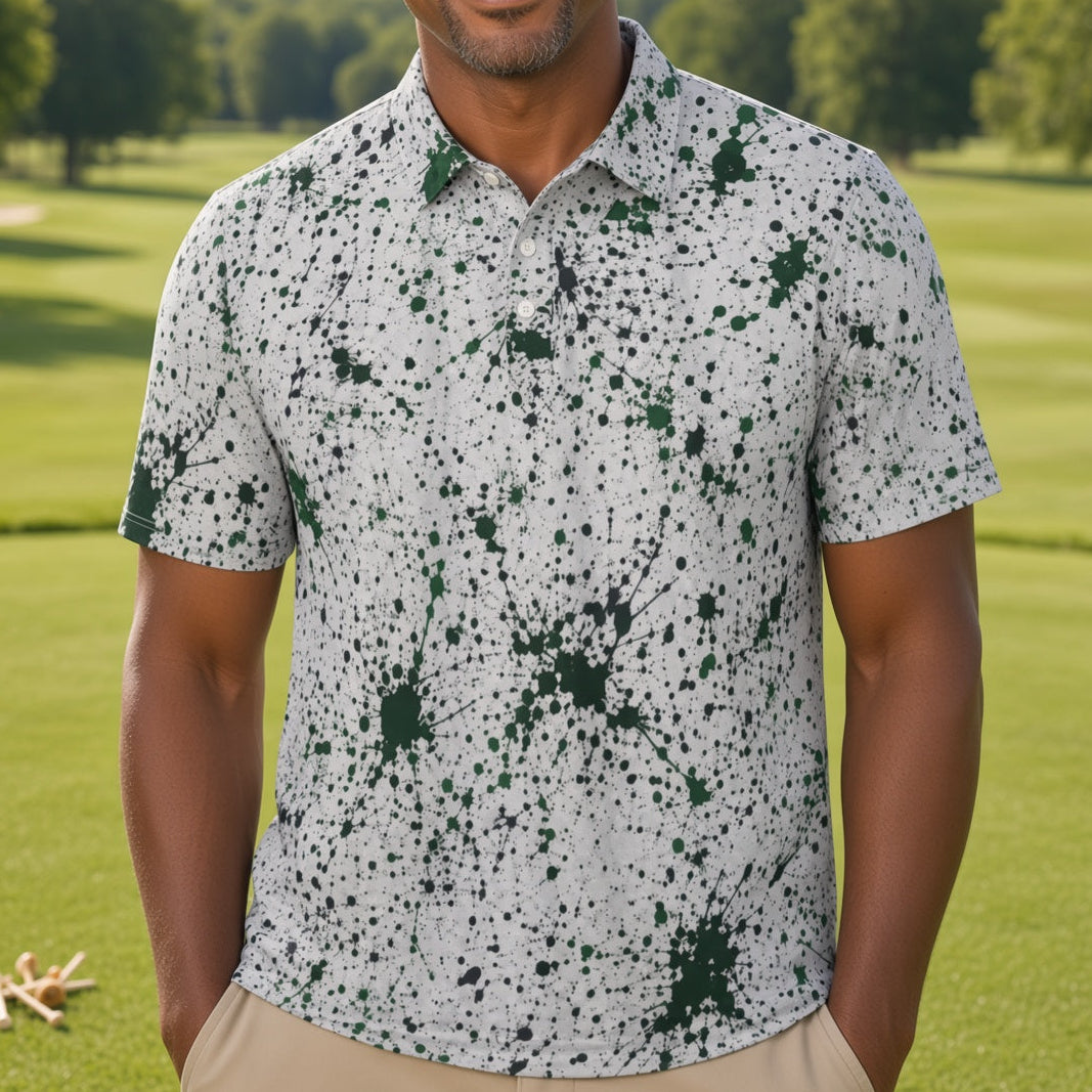 A man smiling on a golf course wearing a white short-sleeve button-up shirt with a dark green and black splatter pattern, paired with khaki pants.