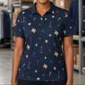 A smiling woman with curly hair stands in a warehouse setting wearing a navy blue short-sleeve polo shirt with a golf-themed print of flags, tees, golf balls, and the state of Texas. Shelves with boxes and other clothing are visible in the background.