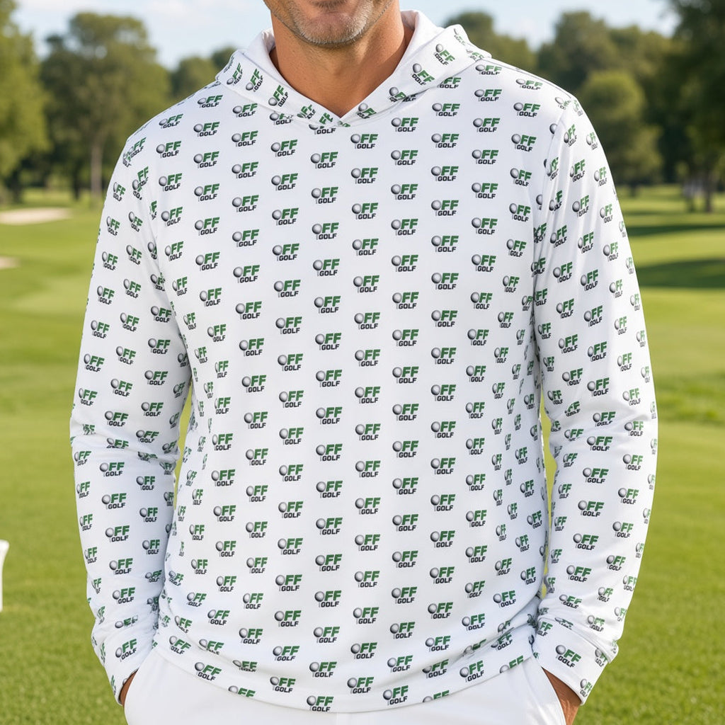 A smiling man stands on a golf course wearing a white long-sleeve hoodie covered in a repeating green crocodile pattern, paired with white pants.
