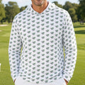 A smiling man stands on a golf course wearing a white long-sleeve hoodie covered in a repeating green crocodile pattern, paired with white pants.