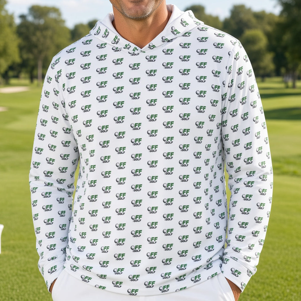 A smiling man stands on a golf course wearing a white long-sleeve hoodie covered in a repeating green crocodile pattern, paired with white pants.