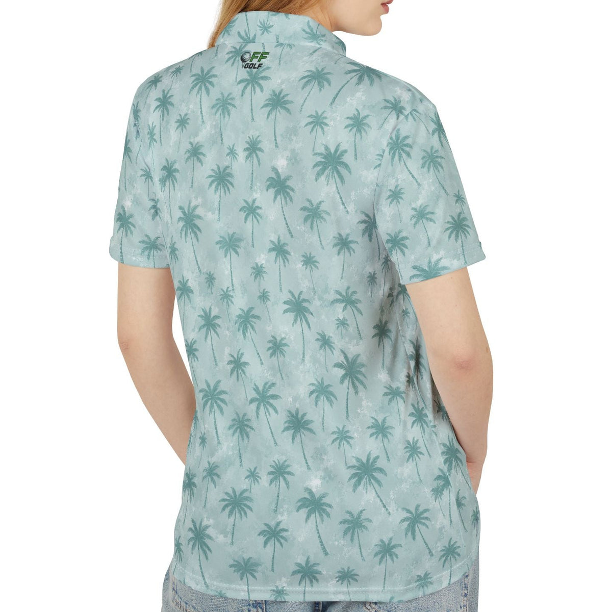 A woman shown from the back wearing a short-sleeve button-up shirt with an all-over teal palm tree print on a light aqua background, paired with light-wash jeans against a plain white studio background.