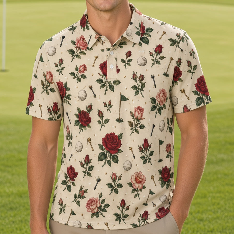 A smiling man stands on a golf course wearing a short-sleeve button-up shirt with a cream base and an allover floral and golf-themed print featuring red roses, green leaves, golf balls, and clubs, paired with khaki pants.